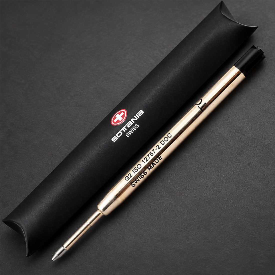 A gold-toned Sottens Swiss pen with a black cap, displayed next to its black cylindrical presentation tube on a dark gray background.