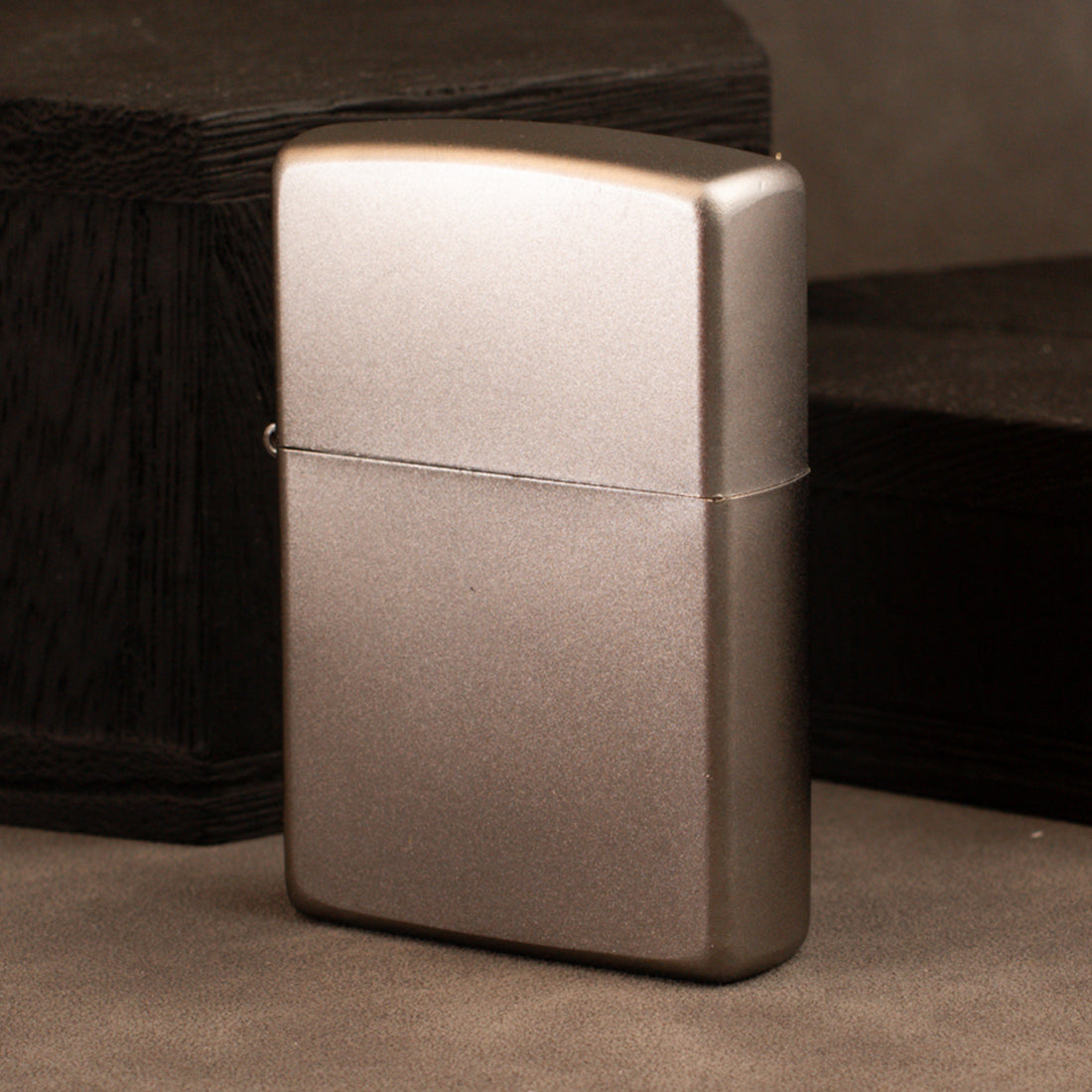 A classic rectangular lighter with a brushed metallic finish, standing upright on a textured surface with dark wooden blocks in the background.