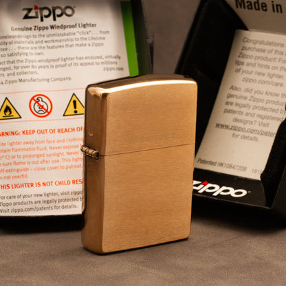 A gold-finished Zippo windproof lighter standing upright on a dark surface, with branded product packaging cards visible behind it.