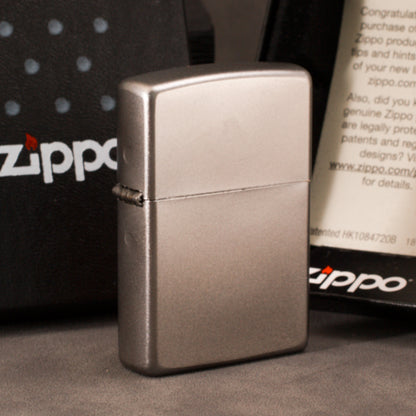 A brushed silver Zippo-style lighter standing upright in front of branded Zippo packaging boxes on a dark surface.