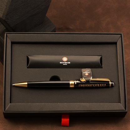 A black and gold pen presented in a black gift box, with a matching black cylindrical pouch behind it. The pen has gold trim, gold lettering reading 'SIMONSCHEEF KUVAKS', and a small Swiss cross logo with the word 'SOVENS' visible on the pouch.