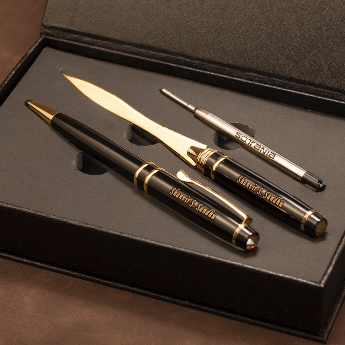 A luxury stationery gift set inside a black presentation box, featuring a black and gold ballpoint pen, a matching gold and black letter opener, and a silver and black precision pen repair tool. The pen and letter opener are engraved with 'Mieru Studio'.