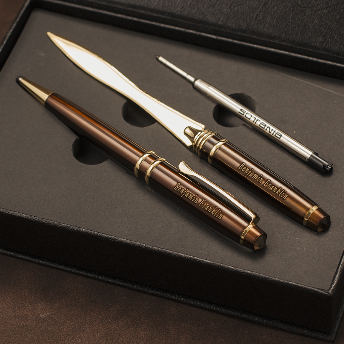 A luxury three-piece writing and stationery set in a black presentation box, featuring a brown and gold ballpoint pen, a silver and gold letter opener, and a silver and gold pencil eraser. The brand 'Briefforts' is clearly engraved on the metal pieces.