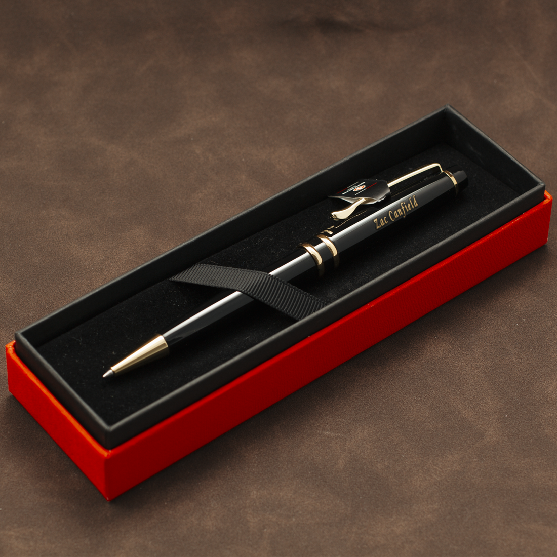 A black ballpoint pen with gold trim and clip, resting inside an open red presentation box with a black velvet interior. The pen has 'EAT CAPITAL' printed on the barrel.