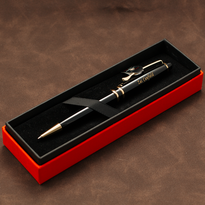 A black ballpoint pen with gold trim and clip, resting inside an open red presentation box with a black velvet interior. The pen has 'EAT CAPITAL' printed on the barrel.