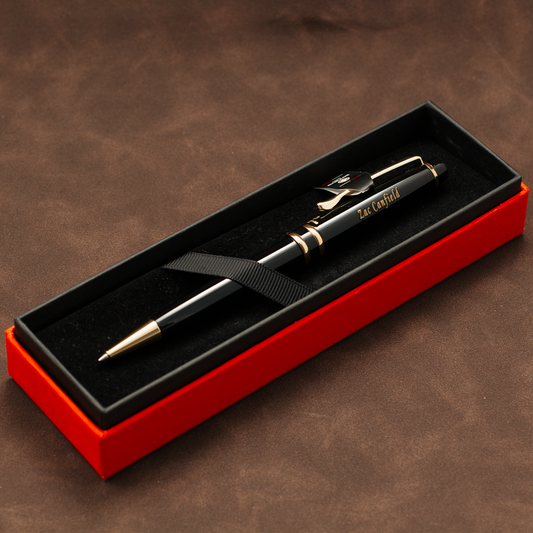 A black ballpoint pen with gold trim and clip, resting inside an open red presentation box with a black velvet interior. The pen has 'EAT CAPITAL' printed on the barrel.