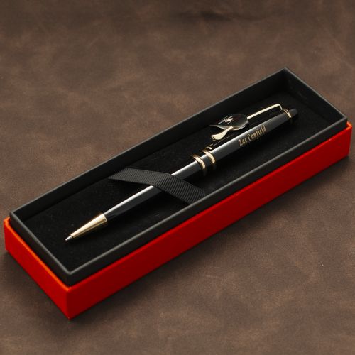 A black ballpoint pen with gold trim and clip, resting inside an open red presentation box with a black velvet interior. The pen has 'EAT CAPITAL' printed on the barrel.