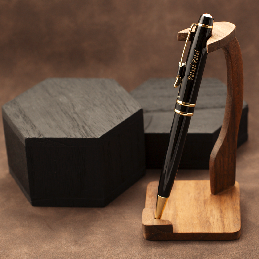 A black ballpoint pen with gold trim and 'Yard Post' printed on the barrel, displayed on a wooden stand against a brown textured background with dark boxes behind it.