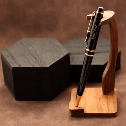 A black ballpoint pen with gold trim and 'Yard Post' printed on the barrel, displayed on a wooden stand against a brown textured background with dark boxes behind it.