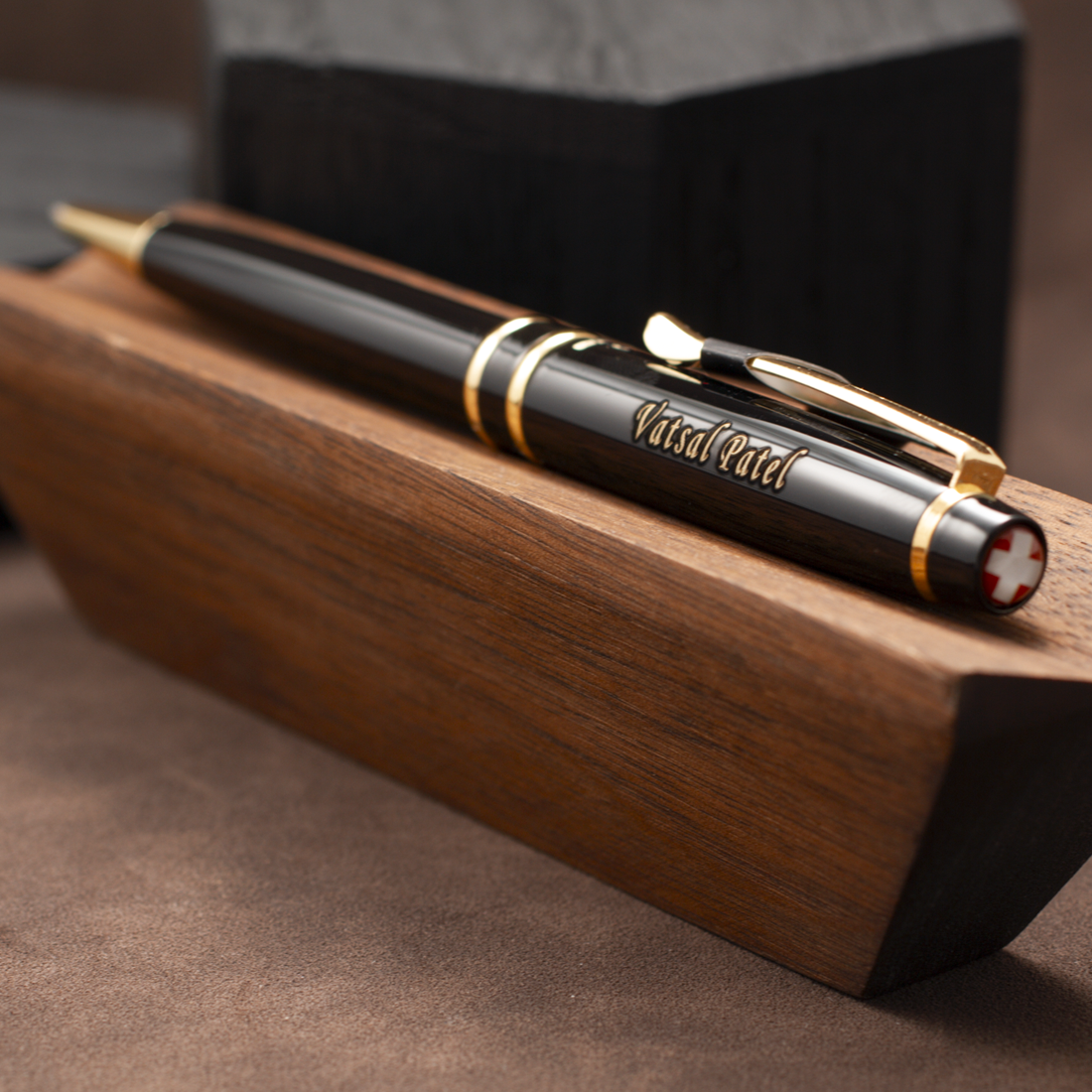 A black and gold pen with 'VisualArt' engraved on the barrel, resting on a polished wooden block.