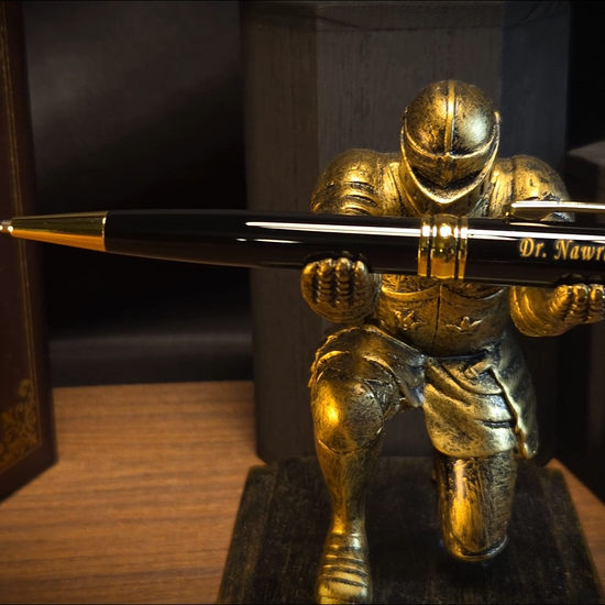 A personalized black and gold pen engraved with 'Dr. Nawras Radwan' inside a blue presentation box next to a silver refill